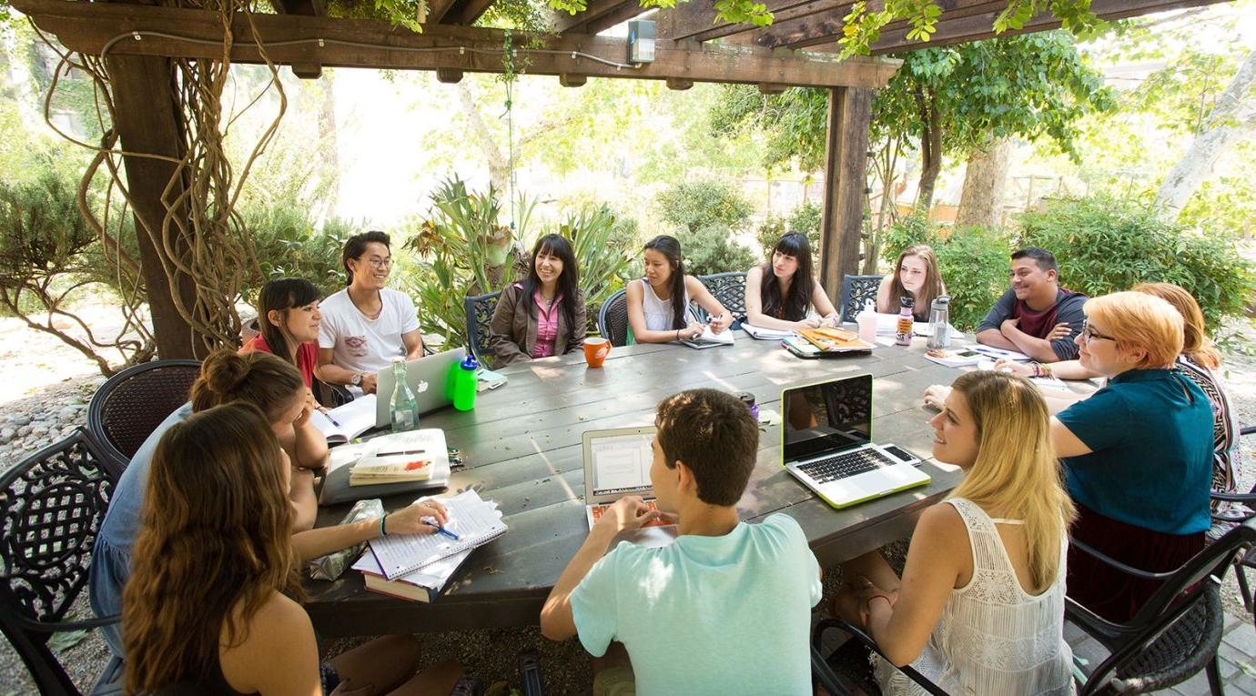 a sociology class and instructor sit in the grove house outdoor classroom